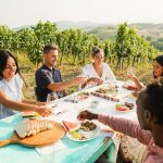 People eating and drinking wine at a table outside in vineyard