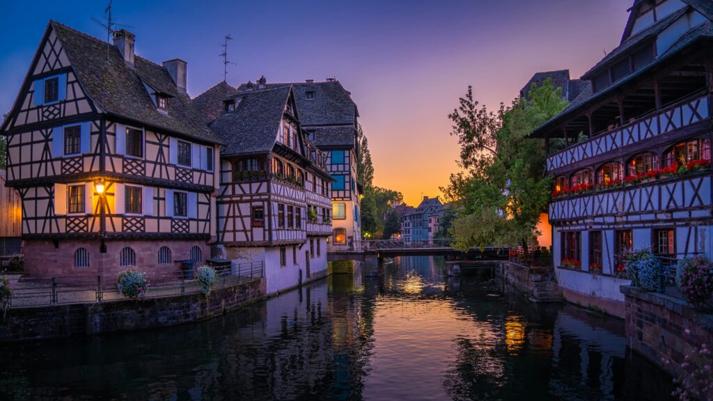 Quaint half-timbered houses along a serene canal in Strasbourg, France, during sunset.