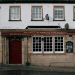 Exterior view of Glenalbyn Bar in Inverness, featuring a whisky-related quote.